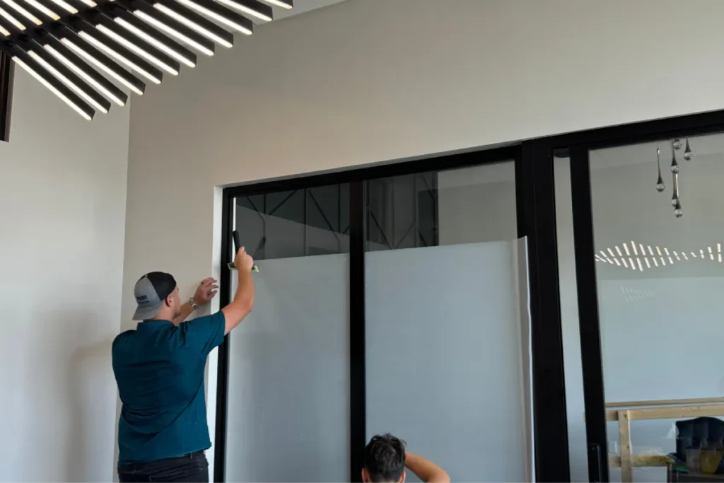 Technician applying frosted commercial window film to an office glass partition